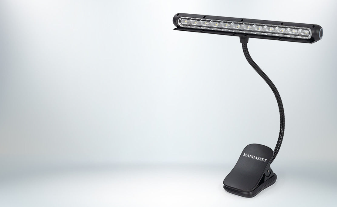 A black clip-on LED light bar lamp with a flexible gooseneck arm and a mounting clip base, shown on a clean light grey studio background. The brand name Manhasset is visible on the base.