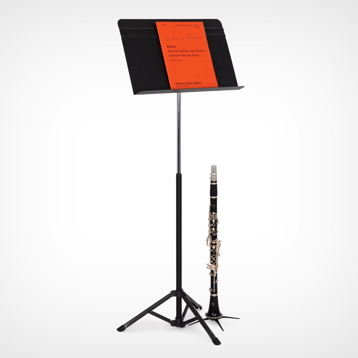 A black metal Voyager music stand holding a sheet music book with a bright orange cover, alongside a black and silver clarinet on a clean white background.